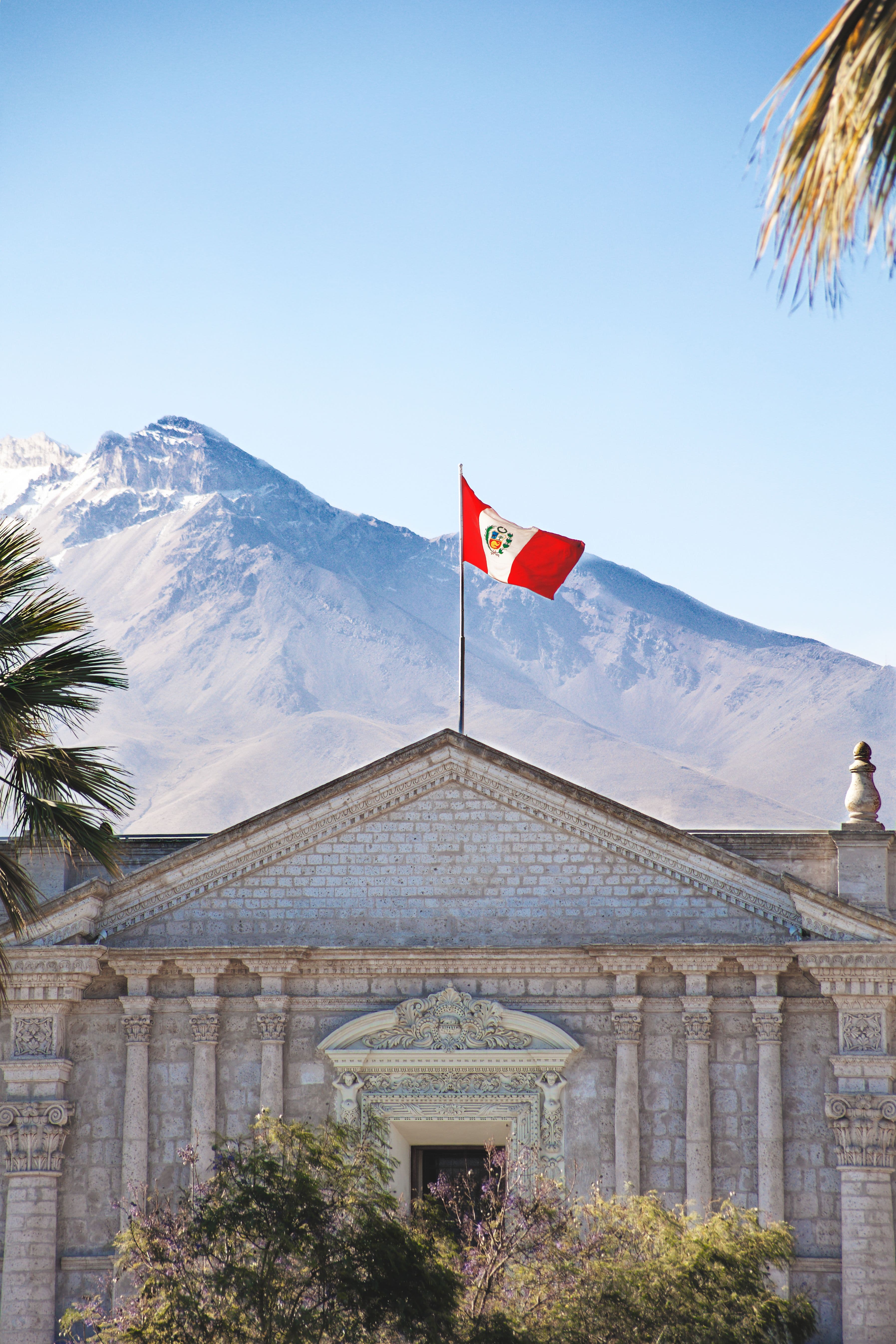 Bandera peruana sobre arquitectura de piedra con montañas al fondo